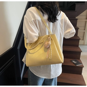 Detailed view of yellow faux leather tote with crocodile pattern and bear plush charm