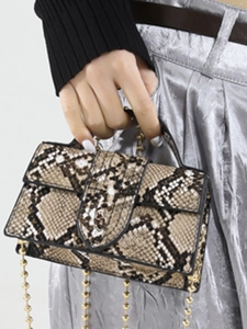 Brown snakeskin mini handbag with gold ball chain strap worn by a model in silver pants