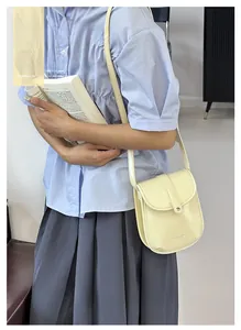 Detail of a creamy yellow mini crossbody bag with a semi-circular flap and leather texture