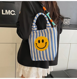 Détail du sac fourre-tout rayé avec patch smiley jaune et bandoulière tissée