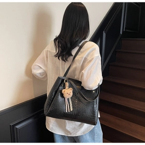 Model wearing a black crocodile pattern tote bag with a brown plush bear keychain