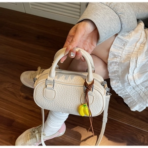Detail of lychee textured cream mini Boston bag with yellow banana charm accessory