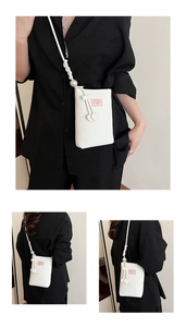 Detail view of white PU leather mobile bag with pearl shoulder strap and heart pendants