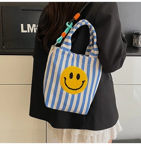 Détail du sac seau en toile à rayures bleues avec un grand patch sourire jaune vif