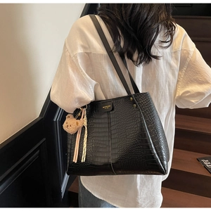 Detail of black faux crocodile leather tote bag with gold rivets and cute bear pendant