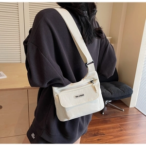 Dettaglio posteriore di una borsa a tracolla in nylon bianco crema indossata da un modello