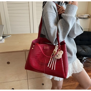 Detail of red croc-embossed tote bag featuring plush bear charm and metallic rivets