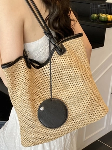 Large beige woven straw tote bag with black leather straps for summer beach vacations