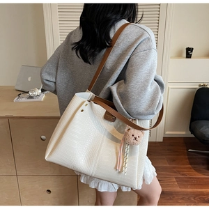 Detailed close-up of large crocodile pattern tote bag with brown straps and cute bear charm