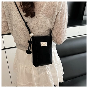 Detail of black glossy crossbody phone bag featuring a large pearl strap and heart charm