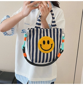 Gros plan du sac à bandoulière en toile rayée avec broderie smiley jaune sur le devant