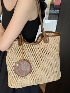 Large hand-woven straw tote bag with brown faux leather straps and circular pendant