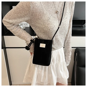 Detail of black mini crossbody bag featuring a ribbon bow and elegant pearl strap accents