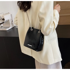 Detailed back view of a black glossy chain shoulder bag on a model wearing a white suit