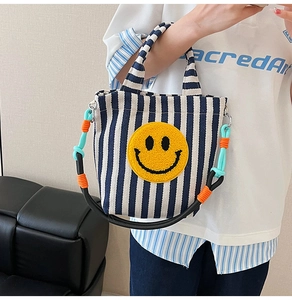 Détail du sac en toile rayé bleu avec smiley en peluche et bandoulière tissée colorée