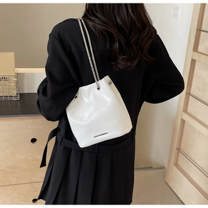 Detail of white bucket bag with silver chain strap on black dress background