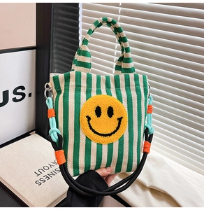 Détail du sac en toile à rayures vertes et blanches avec un écusson smiley jaune pelucheux