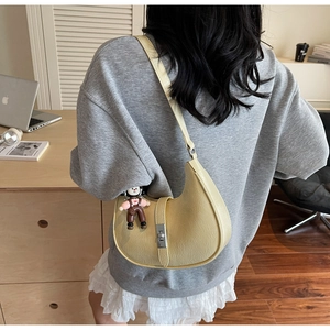Detail of beige half-moon bag with lychee texture and cute doll pendant accessory