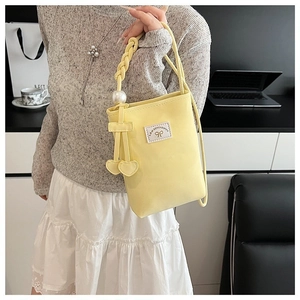 Detail of yellow crossbody bag with pearl strap, woven handle, and heart pendant