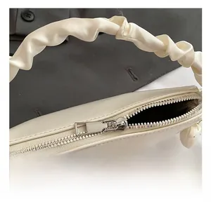 Gros plan du sac à main crème avec fermeture éclair métallique et poignée froncée