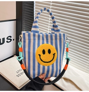 Détail du sac en toile à rayures bleues avec écusson smiley jaune et bandoulière tissée