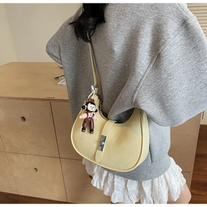 Detail of light yellow leather hobo bag featuring metal buckle and cute charm on the strap