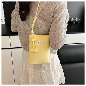 Detail of yellow mini crossbody bag featuring pearl accent and heart charms on model