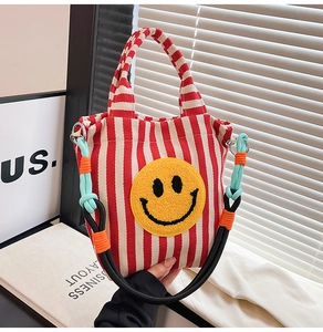 Détail du sac en toile à rayures rouges et blanches avec un patch smiley en peluche jaune