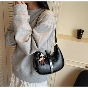 Detail of black pleated faux leather crescent bag with metallic buckle and doll pendant
