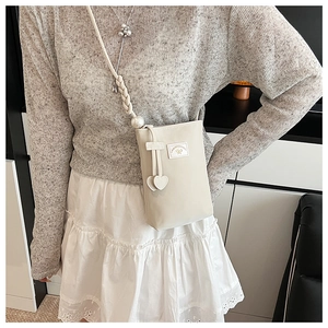 Detail of a creamy white mini crossbody bag with a large pearl accent and woven strap