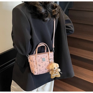 Détail du sac rose avec imprimé ours, plaque logo argentée et peluche sur le cuir