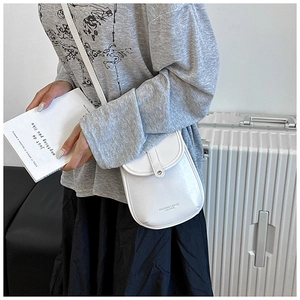 Detail shot of a white leather crossbody phone bag with snap closure in a stylish setting