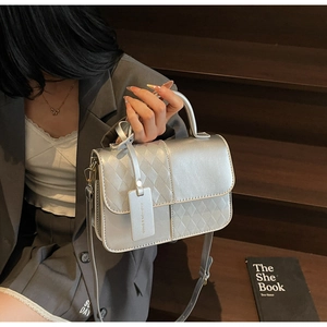 Detail of a silver metallic crossbody bag featuring patchwork texture and a fashion tag