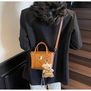 Détail d'un sac à main en cuir PU marron avec un charm ours en peluche sur un escalier en bois