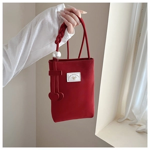 Detail of red small phone bag with woven handle, large pearl and heart charms
