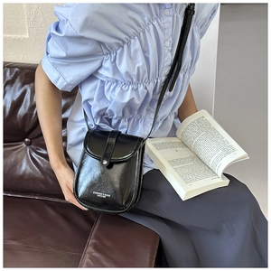 Close-up of a black glossy leather crossbody phone bag shown in a lifestyle setting