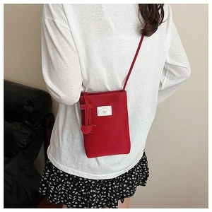 Detail view of red nylon crossbody phone bag with heart pendants and white woven label