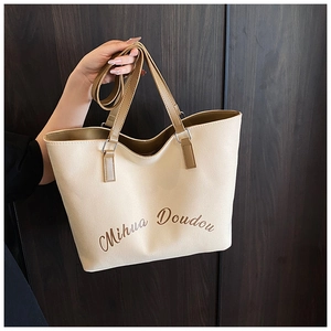 Détail du grand sac cabas en toile avec anses en cuir marron et logo de la marque