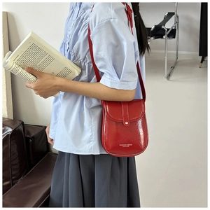 Detail of red patent leather crossbody bag with white fashion text on the front side