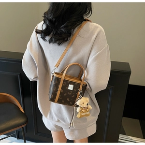 Détail d'un sac bandoulière vintage marron avec monogramme et breloque ours en peluche
