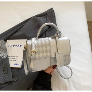 Detail of silver crossbody bag featuring rhombus quilted pattern on a gray blazer