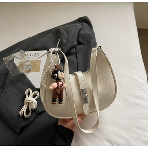 Detail of cream pleated hobo bag with silver clasp, charm, and long strap