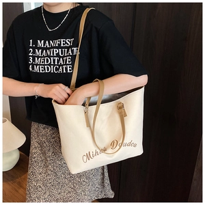 Détail du cabas en toile blanc cassé avec anses en cuir marron et logo de marque
