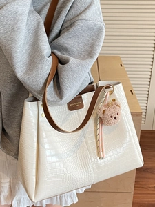 White crocodile pattern tote bag with brown straps and plush bear charm worn by a model