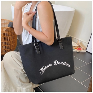 Détail d'un sac cabas en toile noire avec lettrage blanc porté par un mannequin