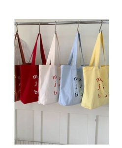 Detail view of colorful canvas tote bags in red, beige, blue and yellow hanging on a metal rack