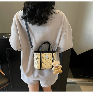 Détail d'un sac à main crème tendance avec imprimé ours et breloque en peluche