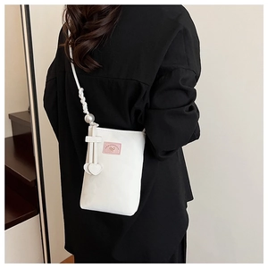 Detail of white crossbody phone bag with pearl strap and pink bow patch accent