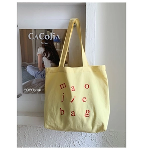 Detail of bright yellow canvas tote bag with red lettering hanging in a modern niche