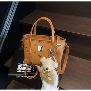 Détail du sac en cuir marron avec motifs papillons et pendentif ours en peluche